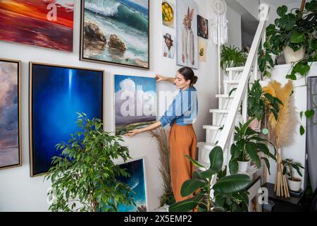 Fokussierte Künstlerin hängte Gemälde an der Wand in der Werkstatt des Studios für kreative Kunst. Stockfoto