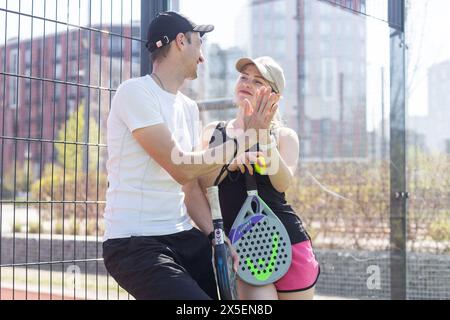 Ukraine Kiew, 02. April 2024. Junge Frau und Mann, die miteinander reden, nachdem sie Padel gespielt haben, und gemeinsam im Netz entlang laufen Stockfoto