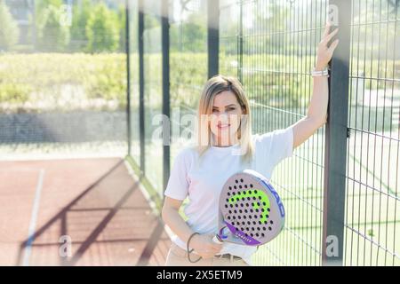 Ukraine Kiew, 03. Mai 2024. Porträt einer lächelnden Frau mit Padel-Tennisschlägerkopf auf dem Hof Stockfoto