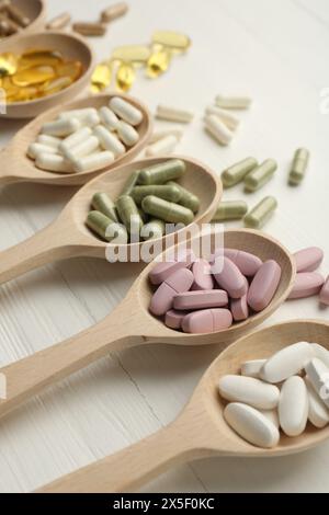 Verschiedene Vitaminkapseln in Löffeln auf weißem Holztisch, Großaufnahme Stockfoto