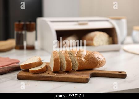 Holzbrotkorb mit frisch gebackenen Broten und Messer auf weißem Marmortisch in der Küche Stockfoto