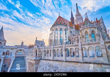 Die prächtige gotische Matthiaskirche hinter der in Stein gemeißelten Arkade der Fischerbastei vor dem hellen Sonnenuntergangshimmel, Budapest, Ungarn Stockfoto