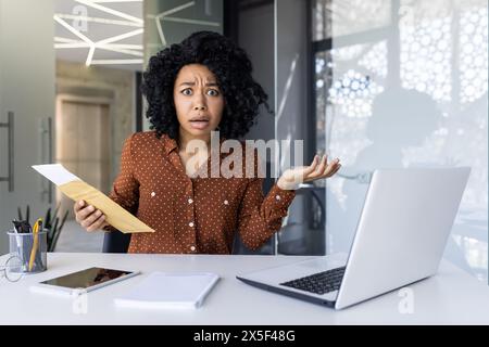 Die afroamerikanische Geschäftsfrau scheint schockiert und beunruhigt zu sein, als sie ein Dokument liest und in einer modernen Büroumgebung Unglauben und Verwirrung ausdrückt. Stockfoto