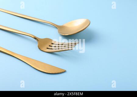 Stilvolles goldenes Besteck auf hellblauem Hintergrund, Nahaufnahme. Leerzeichen für Text Stockfoto