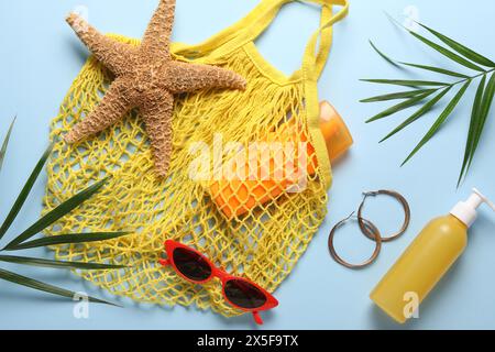 Schnur-Tasche, verschiedene Strandzubehör und Palmblätter auf hellblauem Hintergrund, flach gelegt Stockfoto