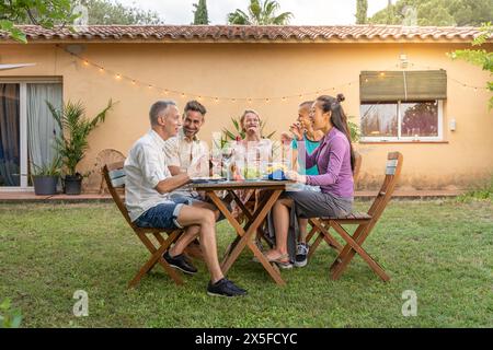 Gruppe von multiethnischen Freunden, die essen und trinken, glücklich lächelnd und lachend auf der Terrasse. Fröhliche Leute mittleren Alters am Tisch. Stockfoto