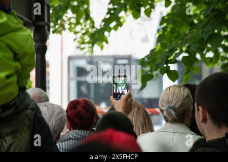 Mann fotografiert ein Straßenfest mit Kameratelefonen. Junger Mann, der mit dem Handy Fotos von Veranstaltungen macht. Rückansicht Stockfoto