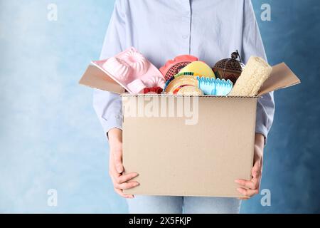 Frau, die eine Kiste mit unerwünschtem Zeug auf blauem Hintergrund hält, Nahaufnahme. Leerzeichen für Text Stockfoto