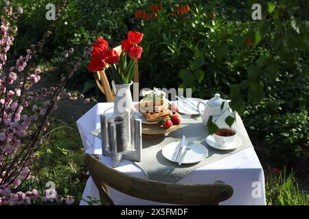 Wunderschöner Tulpenstrauß und frisch gebackene Waffeln auf dem Tisch, serviert zum Teetrinken im Garten Stockfoto