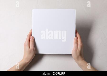Frau, die ein Buch mit leerem Umschlag am weißen Tisch hält, Blick von oben. Modell für Design Stockfoto