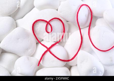 Herz aus Faden auf weißen Kieselsteinen, Draufsicht Stockfoto