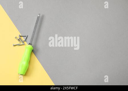 Schraubendreher mit grünem Griff und Schrauben auf farbigem Hintergrund, flach gelegt. Leerzeichen für Text Stockfoto
