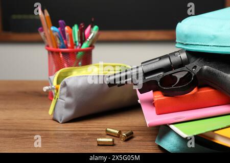 Pistole, Kugeln und Schulpapier auf Holztisch in der Nähe der Tafel drinnen, Nahaufnahme Stockfoto