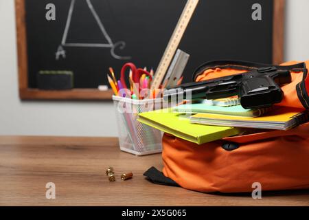 Pistole, Kugeln und Schulpapier auf Holztisch in der Nähe der Tafel drinnen. Leerzeichen für Text Stockfoto