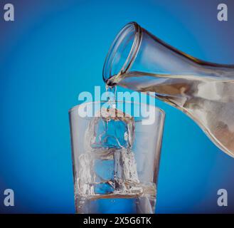 Glas mit Eisfelsen und frischem Wasser, das in das Glas gegossen wird. Stockfoto