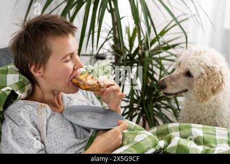 Eine Frau findet Freude in der Gesellschaft ihres Pudels im Bett. Die emotionale Verbindung zwischen Besitzer und Hund Stockfoto