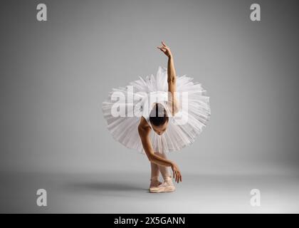 Aufnahme einer Ballerina in voller Länge, die auf grauem Hintergrund tanzt und sich nach vorne lehnt Stockfoto