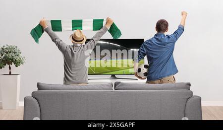 Rückansicht eines jungen und älteren Mannes, der ein Fußballspiel im fernsehen ansieht und zu Hause anfeuert Stockfoto