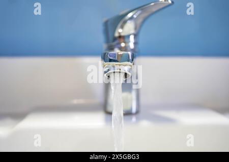 Vorderansicht des Wasserflusses aus dem Waschbecken. Altes Waschbecken mit sauberem Wasser auf blauem Hintergrund. Stockfoto