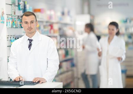 Junger männlicher Apotheker, der am Schreibtisch mit der Tastatur in der Apotheke steht Stockfoto