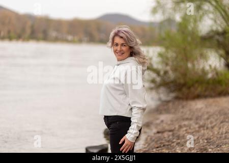 Lächelnde reife Frau, die am Fluss steht. Stockfoto
