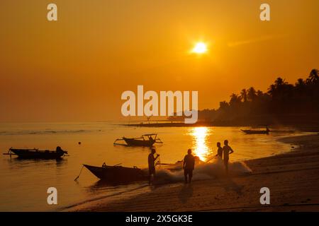 Fischer, ihre Netze und Boote an einem Strand bei Sonnenaufgang in Baucau, der Demokratischen Republik Timor-Leste. Der Dunst am Himmel ist von brennenden Feuern Stockfoto