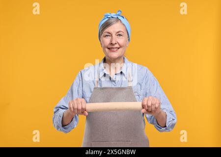 Eine glückliche Hausfrau mit einer rollenden Nadel auf orangem Hintergrund Stockfoto