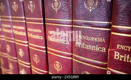 Nahaufnahme einer Reihe von Encyclopaedia Britannica-Bänden, in rotem Leder gebundene Nachschlagewerke mit goldgeprägtem Text in einer Bibliothek Stockfoto