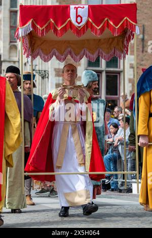 Ein Priester trägt den Glasbehälter mit einem Tuch, das während des katholischen Festes der Prozession des Heiligen Blutes am Himmelfahrtstag mit dem Blut Christi befleckt sein soll. Anlässlich des Himmelfahrt-Tages in Brügge, Belgien, wird die Stadt mit dem jährlichen katholischen fest mit der berühmten Prozession des Heiligen Blutes lebendig. Die Teilnehmer tragen religiöse und historische Kostüme aus, die die Festlichkeit und Pracht der Veranstaltung noch verstärken. Die Straßen verwandeln sich in lebendige Darstellungen des Glaubens und der Tradition, während sich die Prozession durch die Stadt schlängelt und Krähen zieht Stockfoto