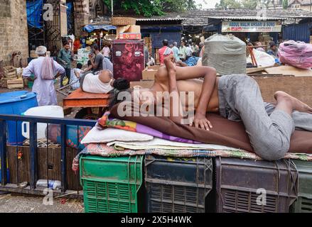 Ein junger Arbeiter auf dem Crawford Market (Mahatma Jyotiba Phule Market) in Mumbai, Indien, der außerhalb des Marktes auf seinem Bett aus Plastikkisten schläft Stockfoto