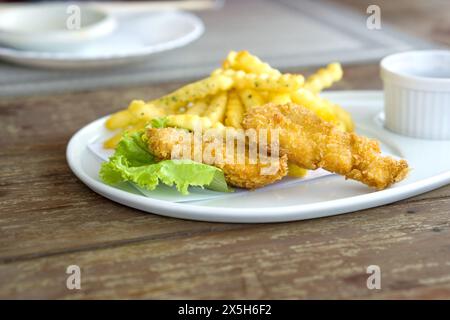 Ein Teller mit knusprigem Fisch, serviert mit goldenen Kartoffelfritten auf einem Holztisch. Stockfoto