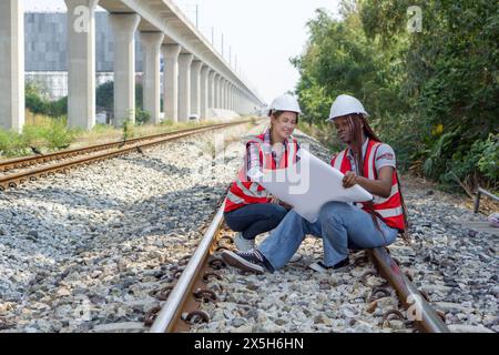 Zwei Konstrukteure oder Ingenieur mit Schutzhelm und Warnweste, die während des Haltens durchzuführende Arbeiten oder Fortschritte bei einem Eisenbahnbauprojekt überprüfen Stockfoto