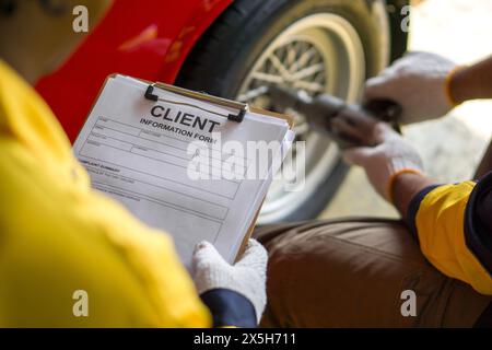 Nahaufnahme Hand mit einem Clipboard mit einem Formular mit Kundendetails, das ausgefüllt werden kann. Ein Mechaniker in Uniform mit einem pneumatischen Schlagschrauber Stockfoto