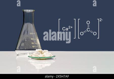 Calciumcarbonatchip in chemischem Uhrglas mit molekularer Struktur auf weißem Labortisch. Seitenansicht Stockfoto