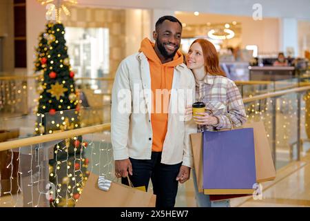 Rabattpreise. Ein lächelndes Paar genießt es, in der Mall zusammen ein rothaariges Mädchen mit Kaffee einzukaufen und ihren Freund mit einem Paar zu sehen, das in S läuft Stockfoto