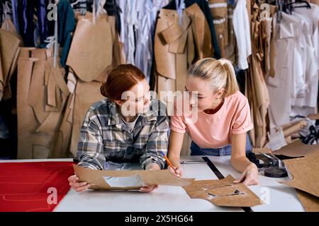 Attraktiver junger Modedesigner und kreativer Partner, der in einem neuen Projekt zusammenarbeitet, kommuniziert, über neue Textilproduktion spricht, braune Kleidung verwendet. In einer modernen Werkstatt Stockfoto