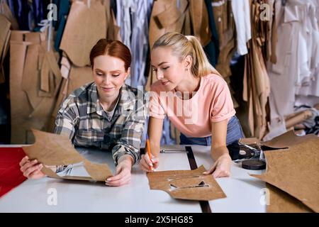 Schöner junger Modedesigner und kreativer Partner, der in einem neuen Projekt zusammenarbeitet, kommuniziert, über neue Textilproduktion spricht, braune Kleidung verwendet. In einer modernen Werkstatt Stockfoto