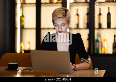 Eine professionelle junge Frau konzentriert sich auf ihre Arbeit auf einem Laptop in einer gemütlichen Café-Umgebung und zeigt Konzentration und Entschlossenheit. Stockfoto