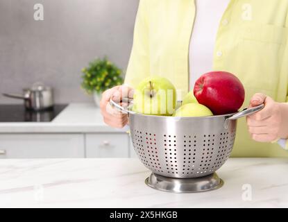 Frau, die ein Sieb mit frischen Äpfeln an einem weißen Marmortisch in der Küche hält, Nahaufnahme. Leerzeichen für Text Stockfoto