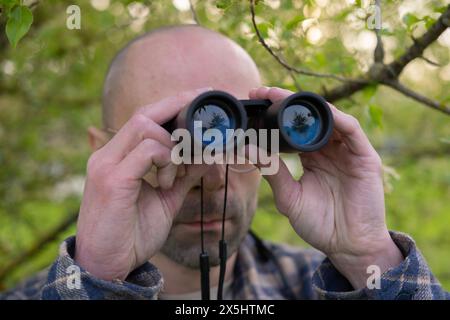 Junger Mann, versteckt in üppigem Grün, Spione bekleidet durch Ferngläser, versteckte Operationen, Nervenkitzel-Sucher-Suche-Ziel Stockfoto