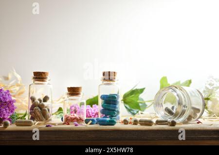 Natürliche Labormedikamente mit Kapseln und Pillen in Glasflaschen mit Pflanzen und Blumen auf Holztisch und weißem isolierten Hintergrund. Vorn V Stockfoto