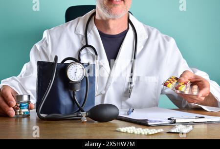 Arzt verschreibt Blutdruckmedikamente mit mehreren Blisterpackungen in den Händen auf einem hölzernen Bürotisch mit Blutdruckmessgerät Ordner und mehr Stockfoto