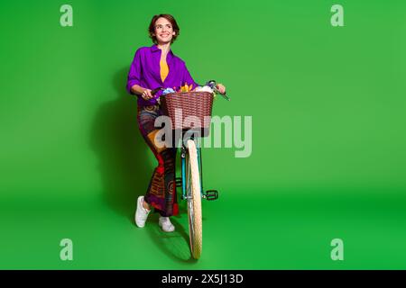 Foto der lustigen jungen Frau tragen lila Hemd und braunen bob Haarschnitt warten mit Fahrrad im Sommer isoliert auf grünem Farbhintergrund Stockfoto