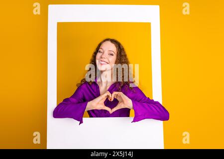 Foto der schönen jungen Dame Instant Fotorahmen zeigen Herz Geste gekleidet stilvolles violettes Kleid isoliert auf gelbem Farbhintergrund Stockfoto