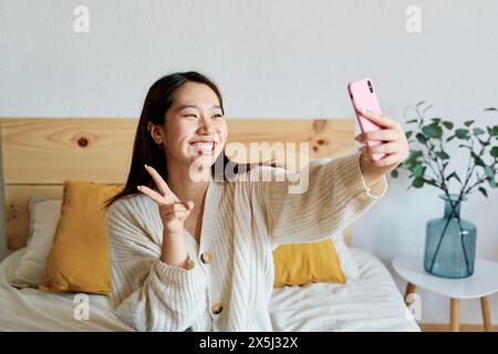 Eine Frau sitzt auf einem Bett und macht ein Selfie mit einem Smartphone Stockfoto