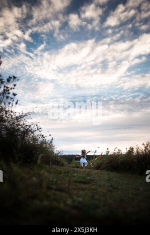 Ein kleines Mädchen, das unter blauem Himmel durch Gras läuft Stockfoto