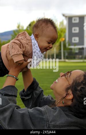Schwarze Mutter hebt das lachende Baby in einem freudigen Outdoor-Binding-Moment Stockfoto