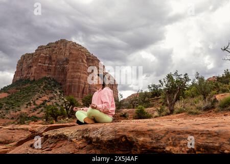 Frau, die unter stürmischem Himmel meditiert, sitzt auf dem Berg Stockfoto