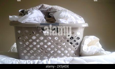 Wäschekorb gefüllt mit weißer Bettwäsche auf einem Bett Stockfoto
