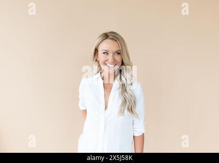 Lächelnde Frau in weißem Hemd auf pfirsichbraunem Hintergrund Stockfoto